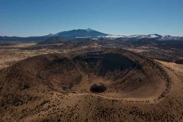 Drone photo of Colton Crater, an ancient volcano in northern Arizona, with the San Francisco Peaks in the distance.